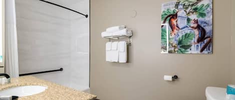 Un baño con lavamanos de encimera de granito, un inodoro blanco, un perchero con toallas dobladas y un cuadro de un gato en una rama de árbol.