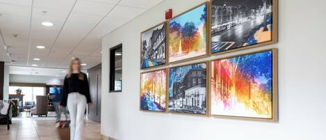 A hallway with six framed photographs on the wall, a person walking, and a television in the background.