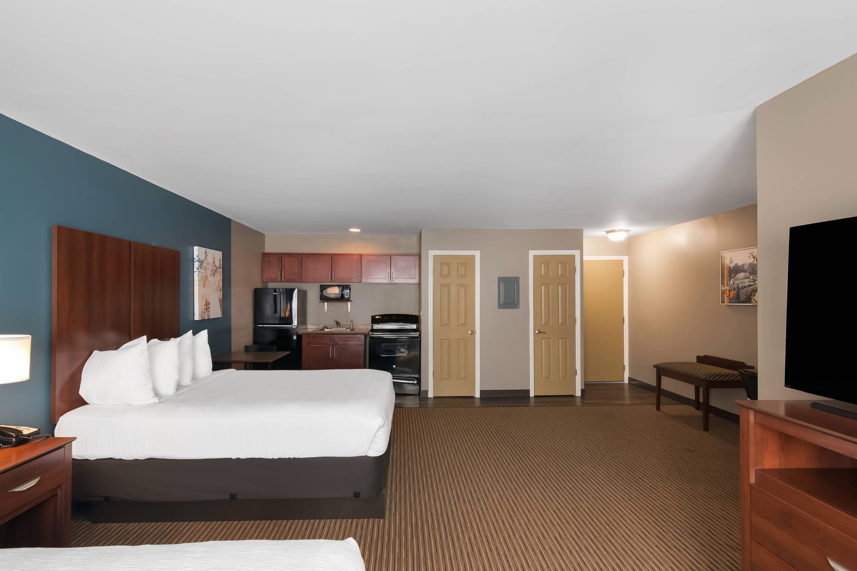 Quarto de hotel com cama grande, escrivaninha, televisão, cozinha compacta e banheiro.