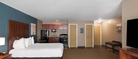 Une chambre d’hôtel avec un grand lit, un bureau, une télévision, une kitchenette et une salle de bain.