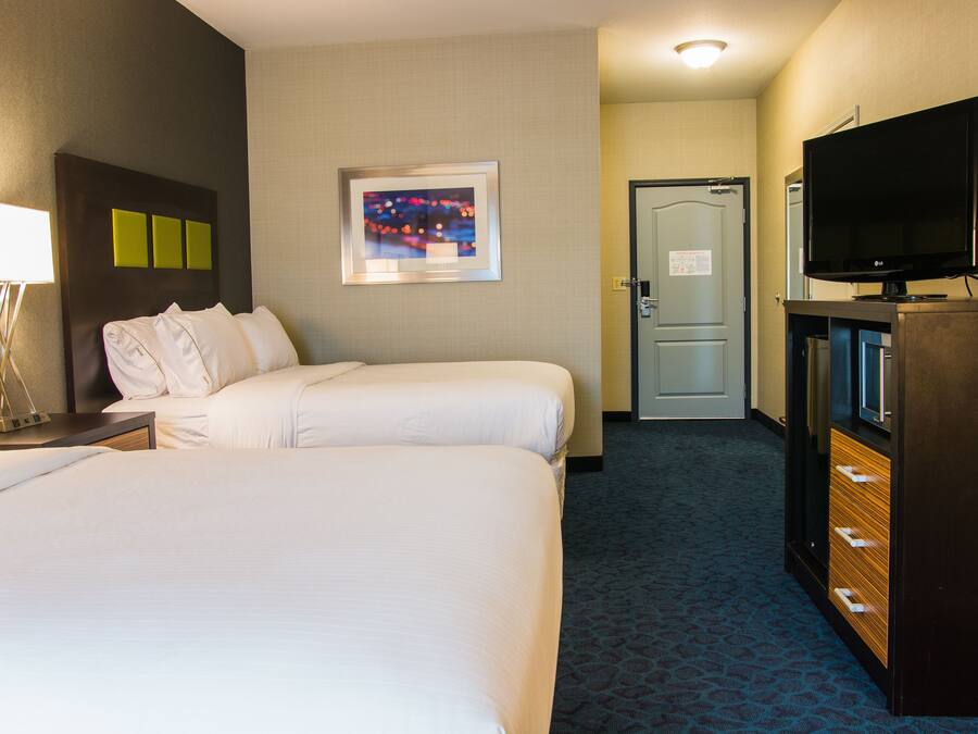 A hotel room with two beds, a television, a desk with a lamp, and a door leading to another room.