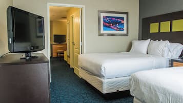 Habitación de hotel con televisor sobre un escritorio, una cama, una puerta que da a un pasillo y un cuadro en la pared.