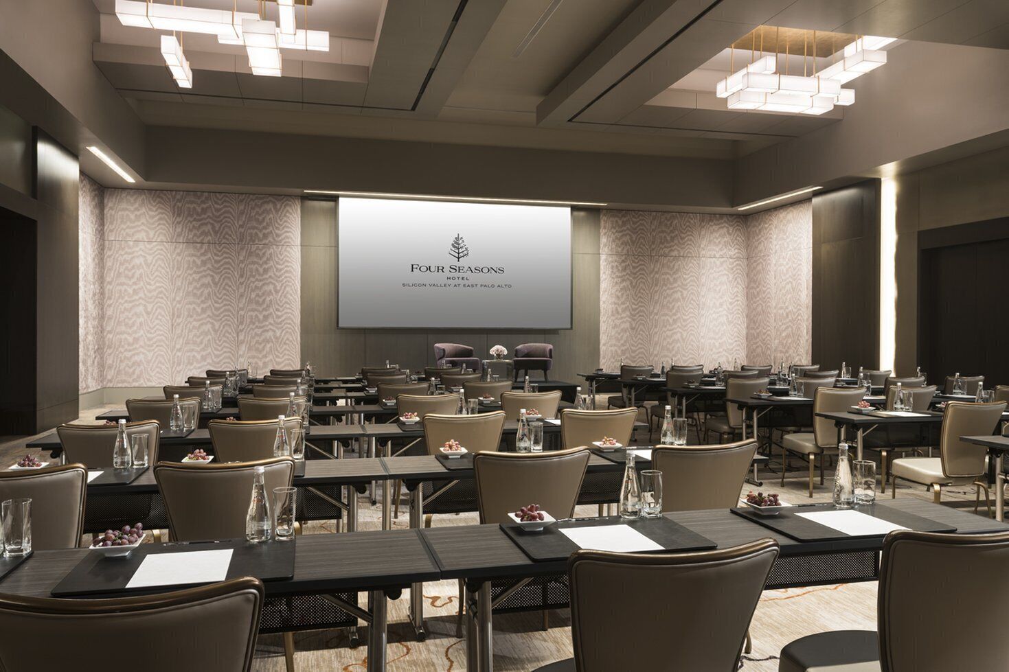 Ein Konferenzraum im Four Seasons Hotel mit einer großen Leinwand, die den Namen des Hotels zeigt, mehreren Tischen mit Stühlen und einer modernen Kristallleuchtre.