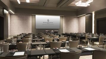 Ein Konferenzraum im Four Seasons Hotel mit einer großen Leinwand, die den Namen des Hotels zeigt, mehreren Tischen mit Stühlen und einer modernen Kristallleuchtre.