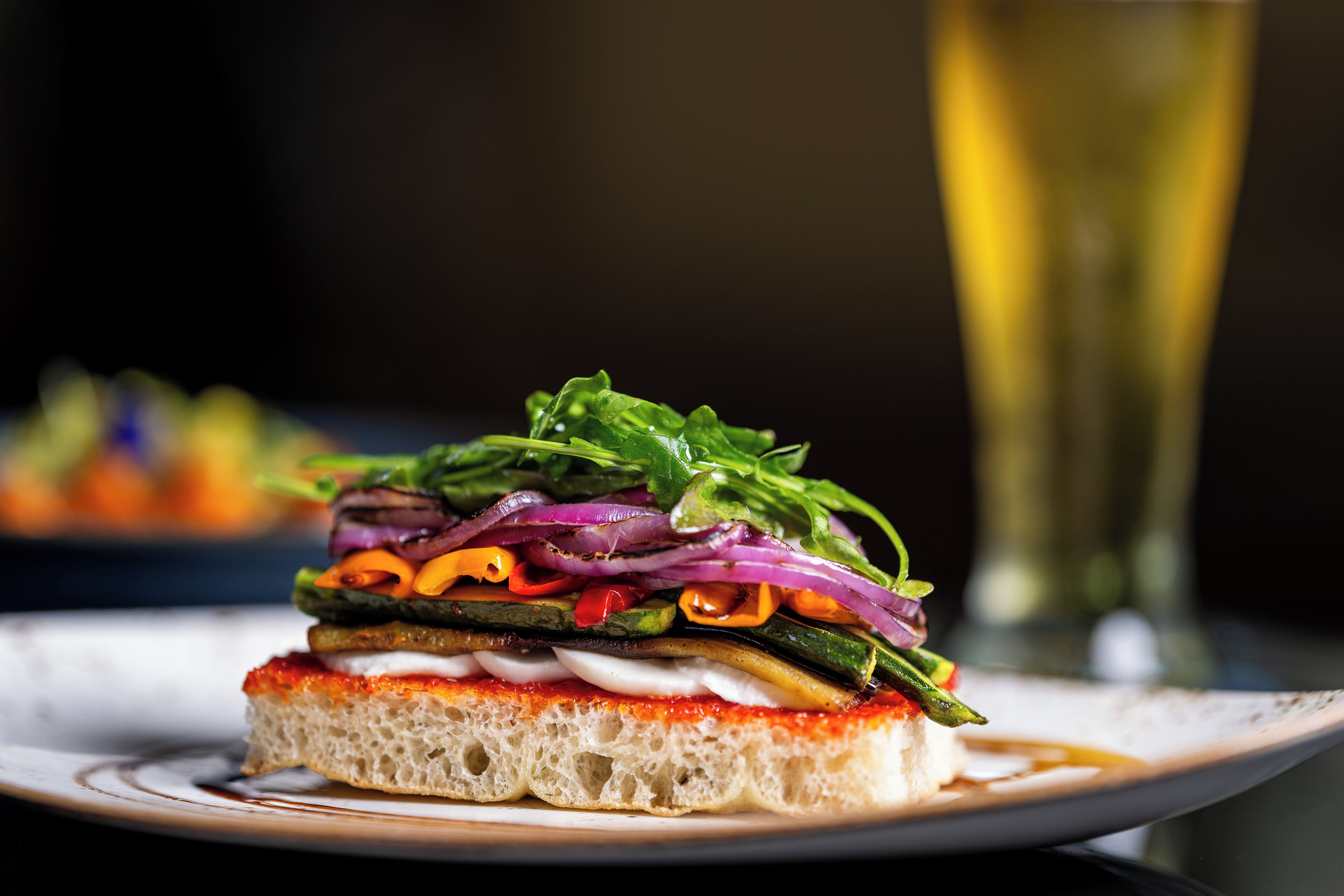 Ein Sandwich mit verschiedenen Gemüsesorten und ein Glas Weißwein auf einem Teller.