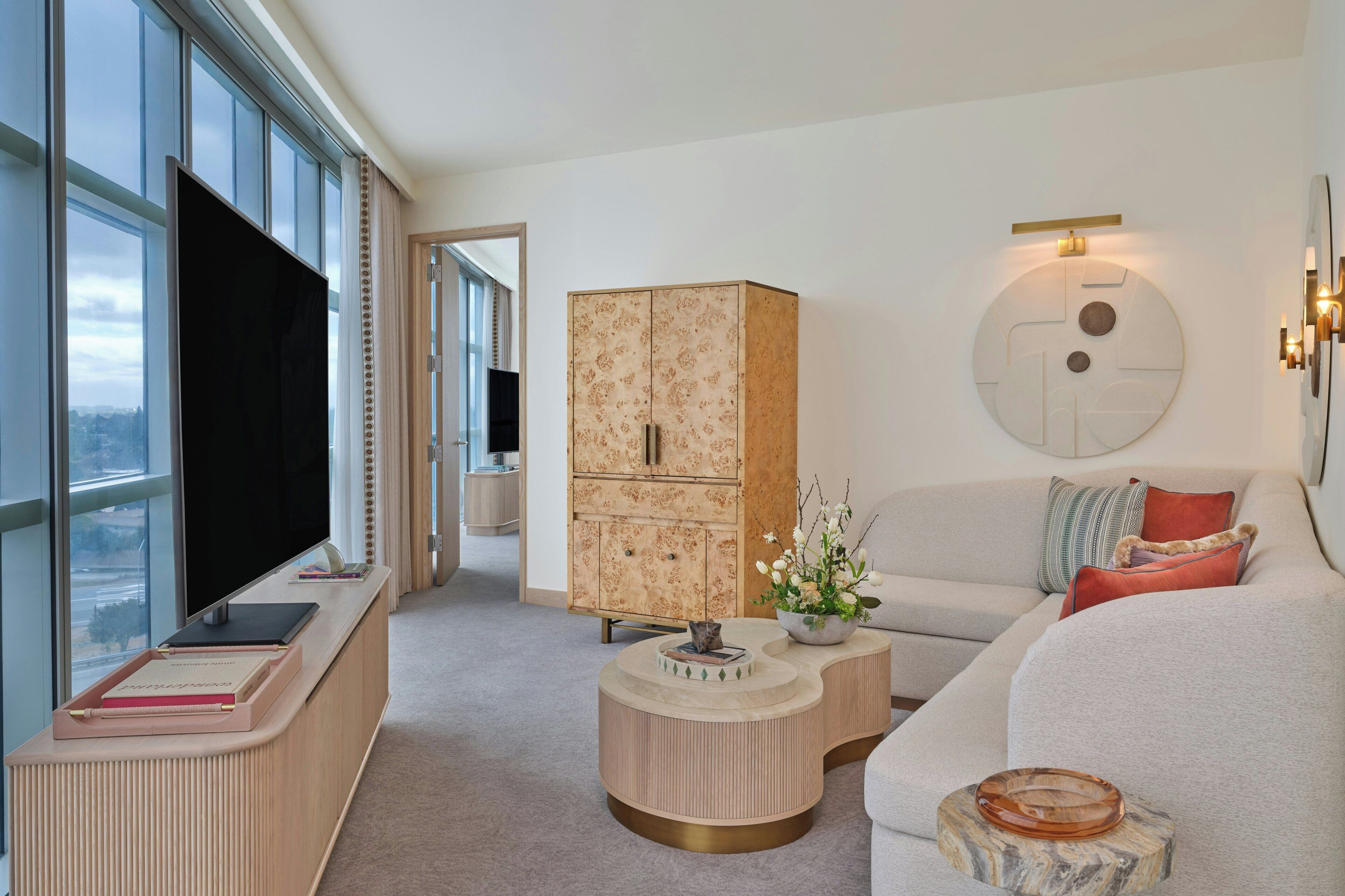 Een moderne woonkamer met een grote flatscreentelevisie, een houten kast, een ronde salontafel en een bank met decoratieve kussens.