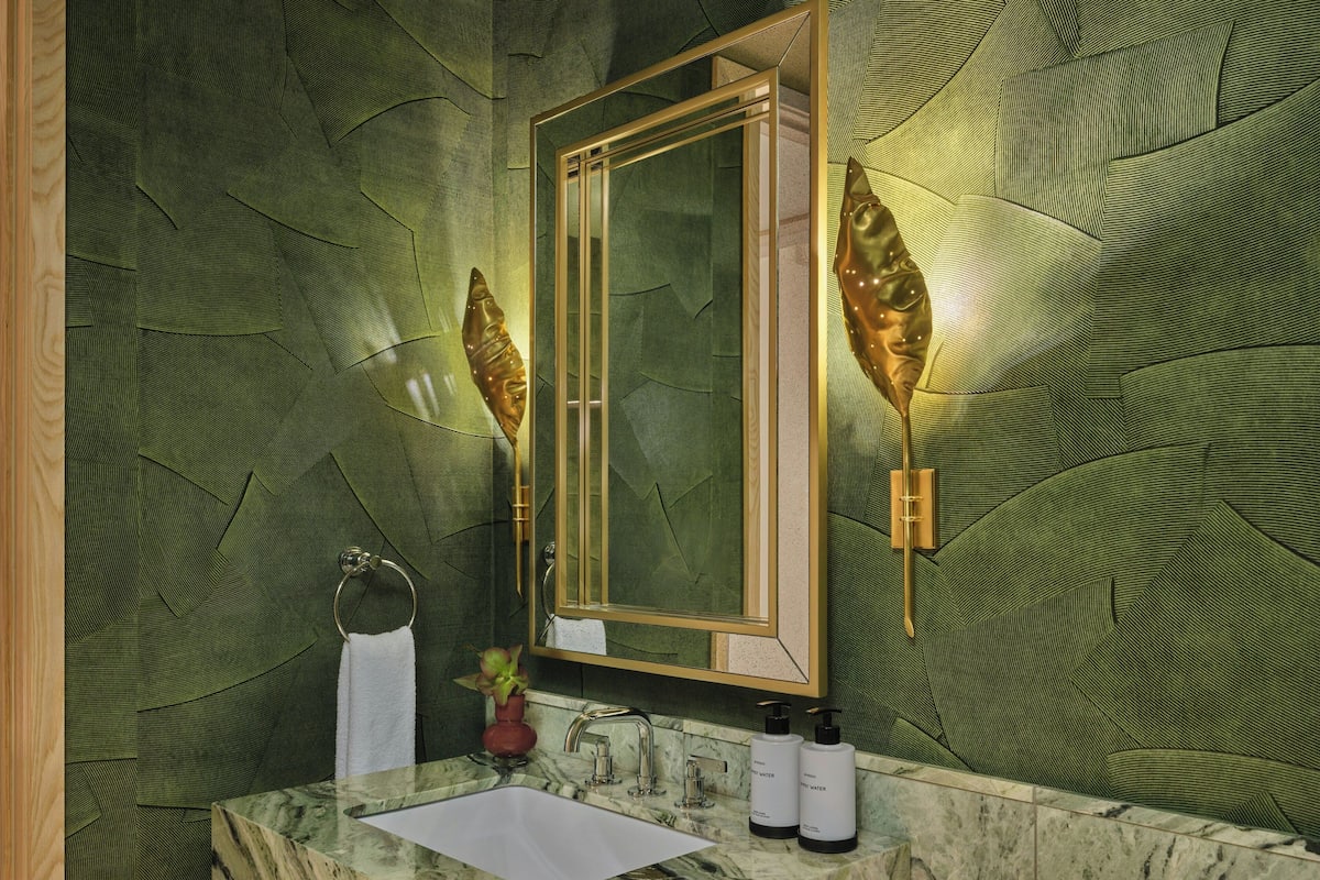 Ein Badezimmer mit Marmorwaschbecken, einem goldfarben gerahmten Spiegel und rauen, grünen Wänden.