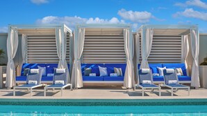 A poolside area with a blue sofa and lounge chairs, a tiled pool, and a clear sky.