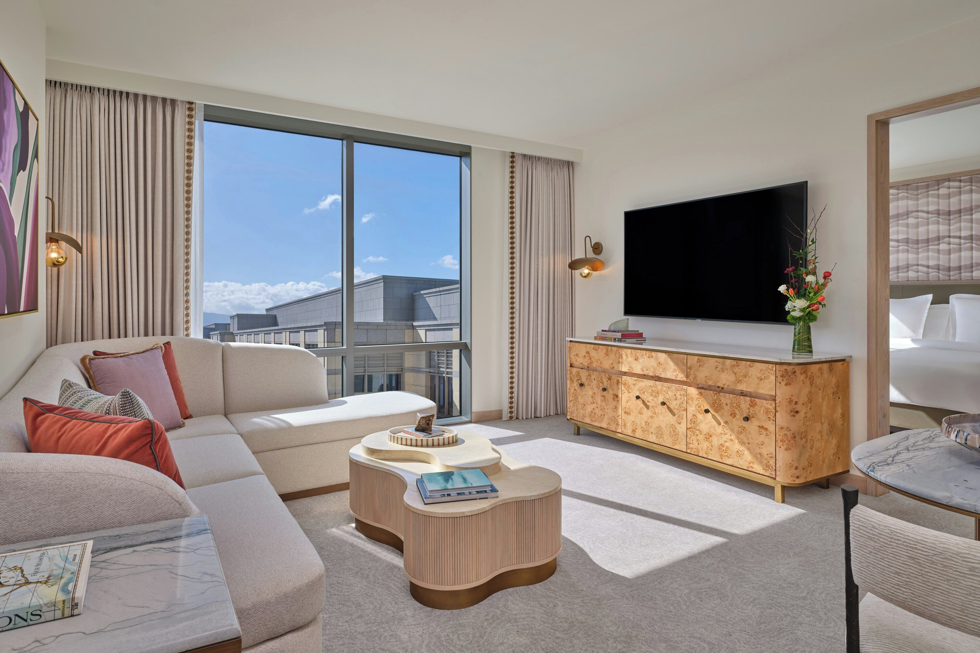 Une chambre d’hôtel moderne dotée d’une grande fenêtre, d’un canapé, d’une table basse, d’un téléviseur et d’une armoire en bois.
