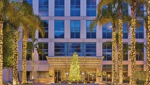 A modern hotel with a large entrance, palm trees, and festive lights.