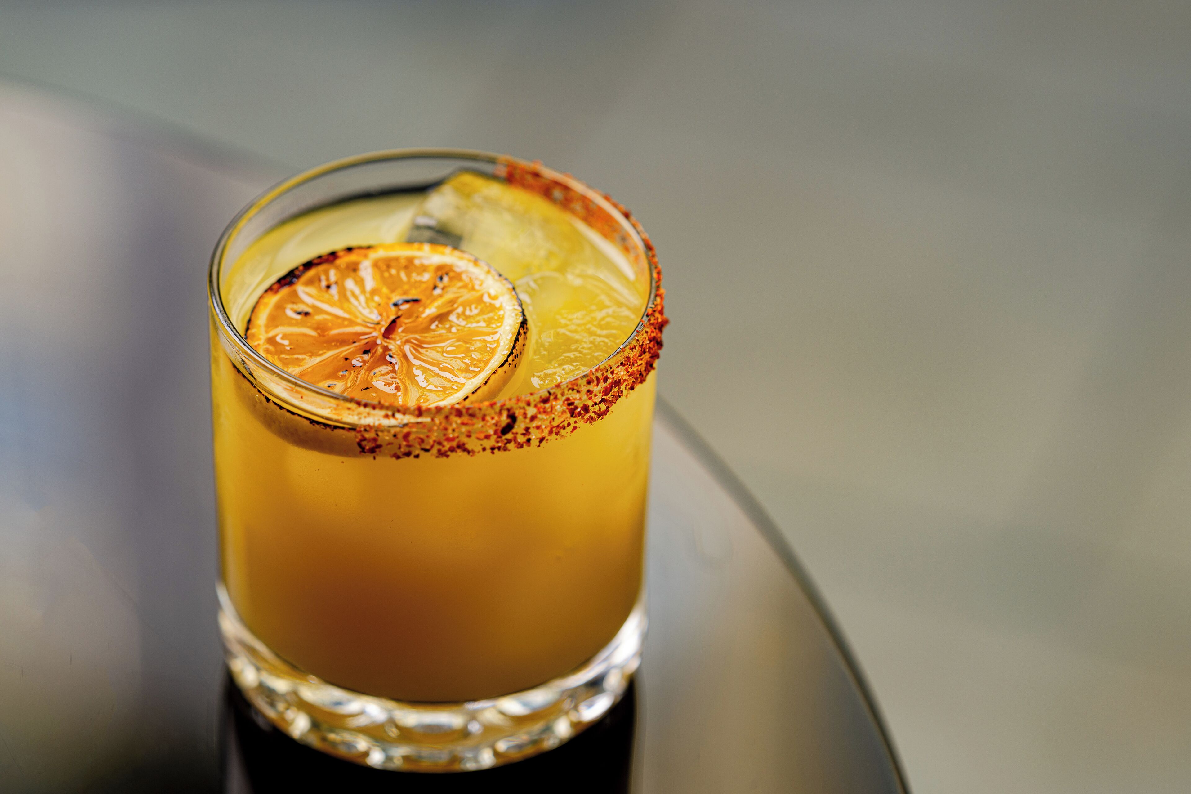 Ein Glas mit einem orangen Getränk, einer Orangenscheibe als Garnitur und einem Rand, der mit rotem Gewürz bestreut ist.