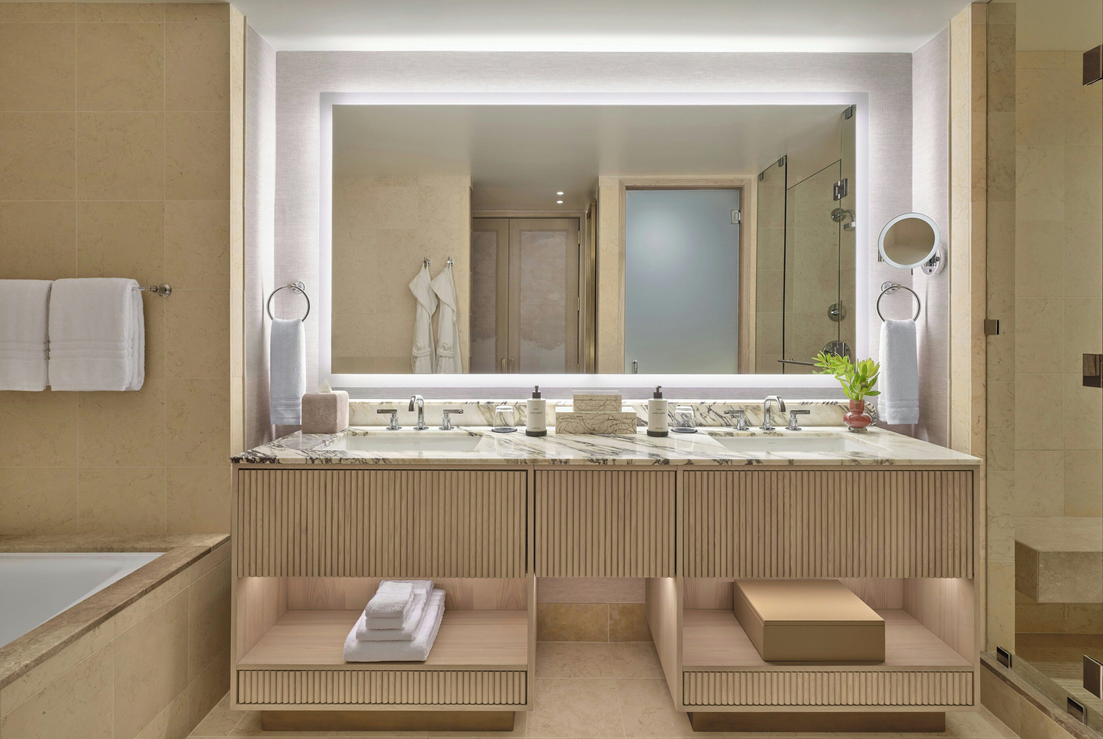 A modern bathroom with a large mirror, dual sinks, a bathtub, and a vanity with storage.