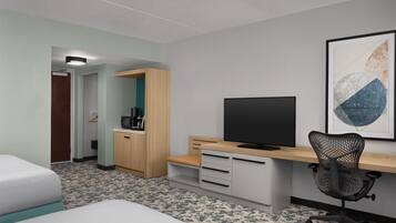 A hotel room with a bed, a desk with a computer, a chair, a TV, and a framed artwork on the wall.