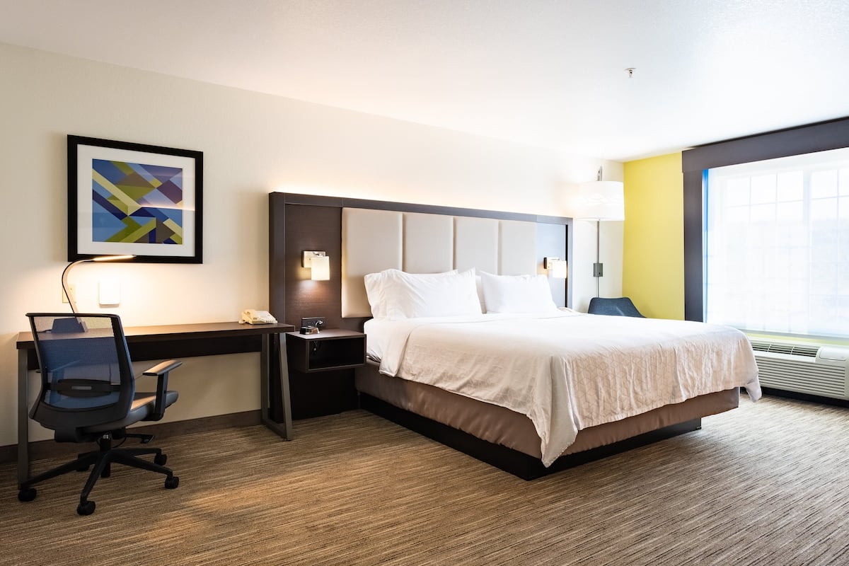 Una habitación de hotel con cama, escritorio, silla y una obra de arte en la pared.