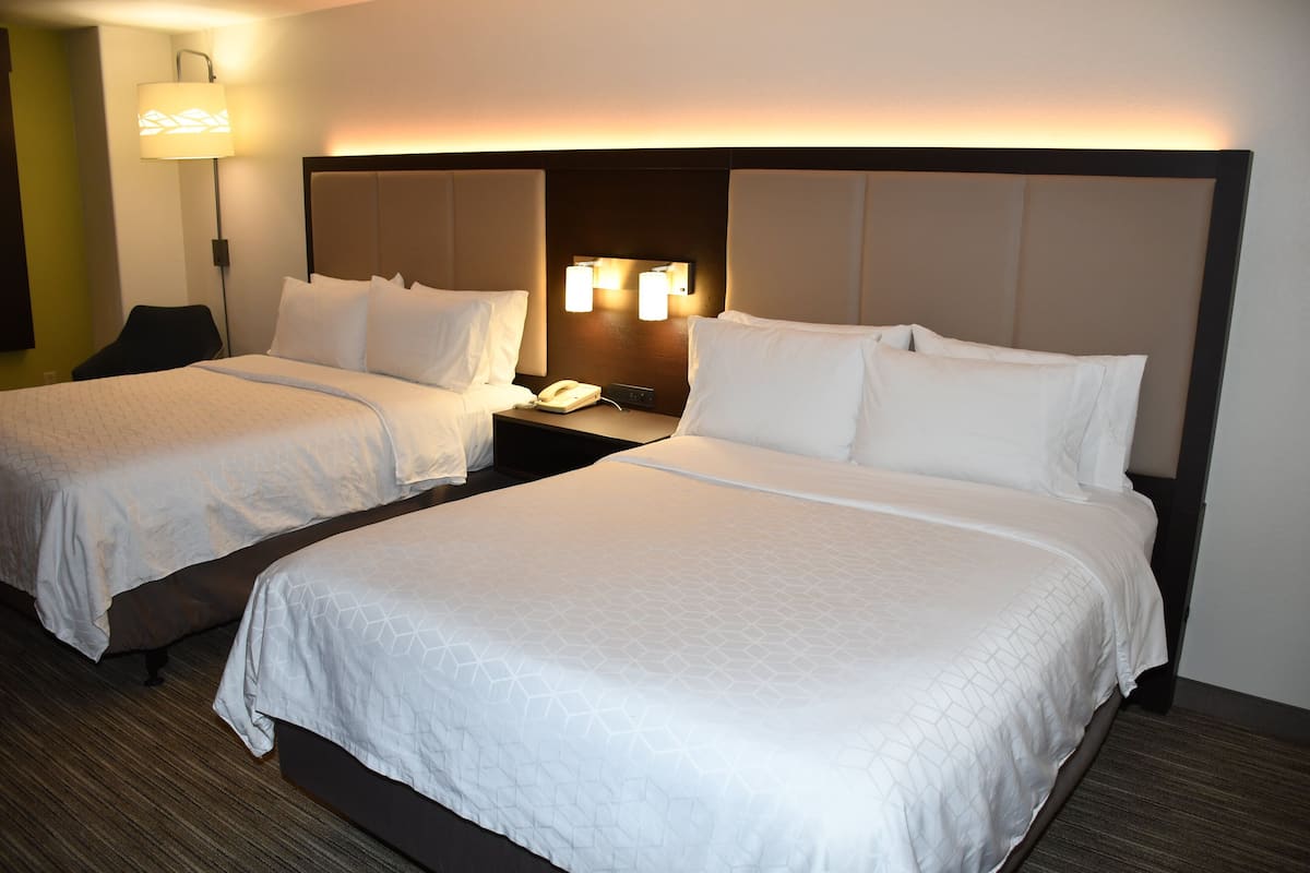 Habitación de hotel con dos camas, una mesita de noche con teléfono y una lámpara de pared.