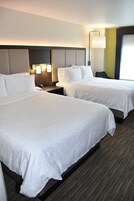 Habitación de hotel con dos camas, una mesita de noche, una lámpara y un aplique de pared.