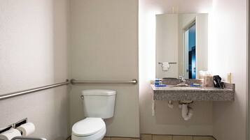 A small bathroom with a toilet, a handrail, a sink with a mirror, and a towel rack.