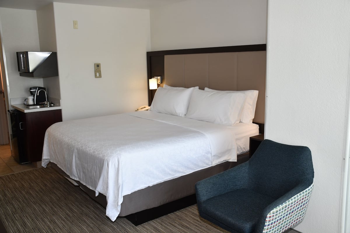 Una habitación de hotel con una cama grande, una mesita de noche con una lámpara y una silla.