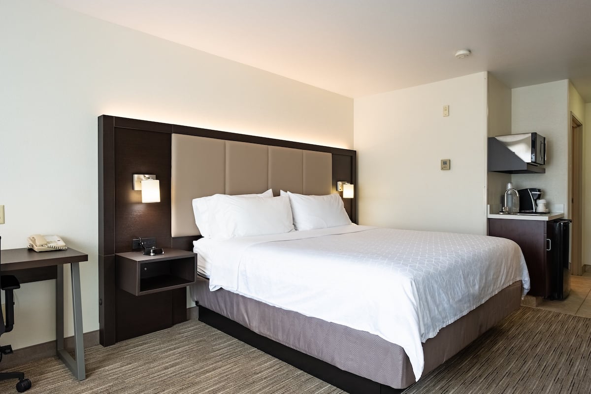 Habitación de hotel con una cama grande, un escritorio con teléfono, una mesita de noche y un televisor sobre un mueble.