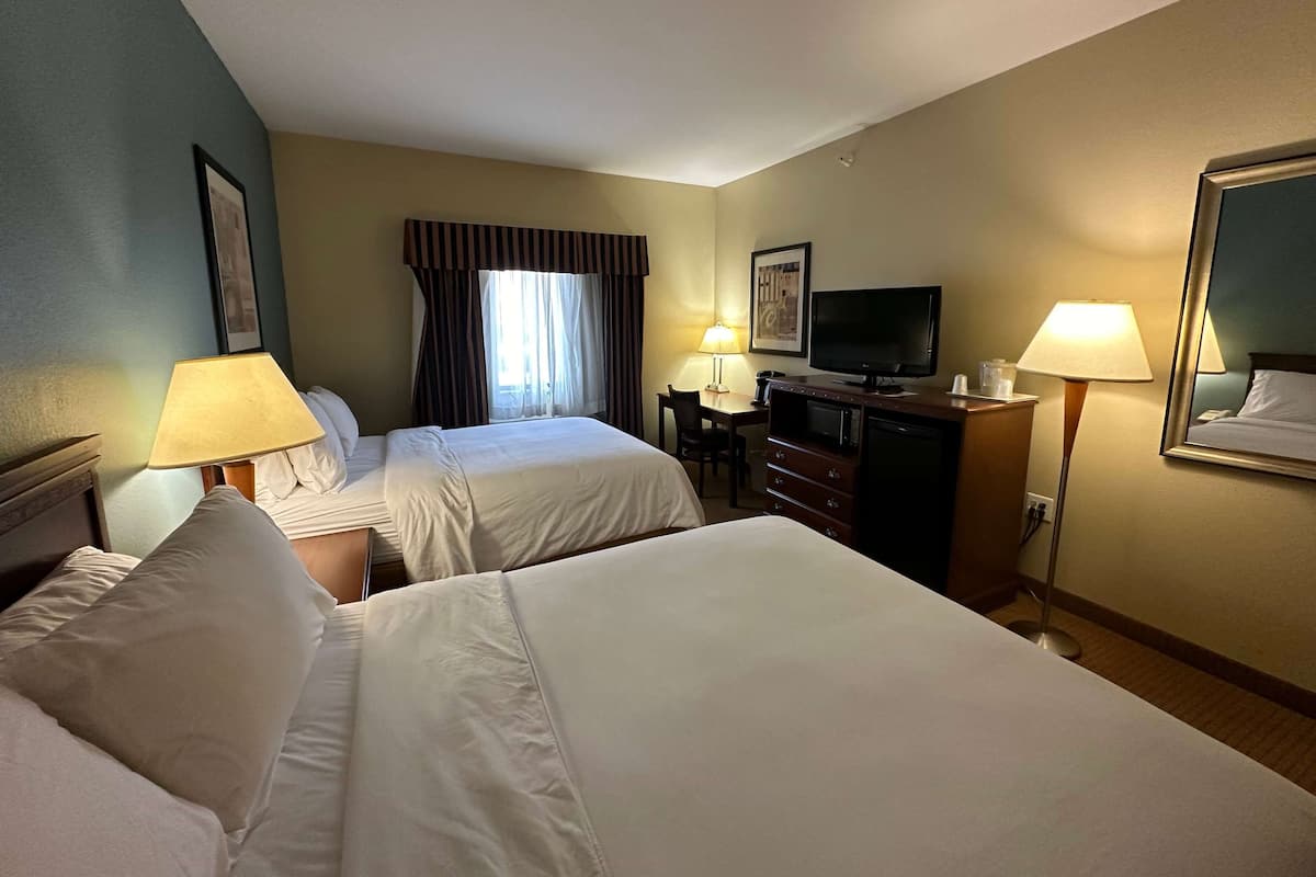 A hotel room with two beds, a desk with a television, a dresser, and two lamps.