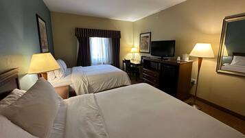 A hotel room with two beds, a desk with a television, a dresser, and two lamps.