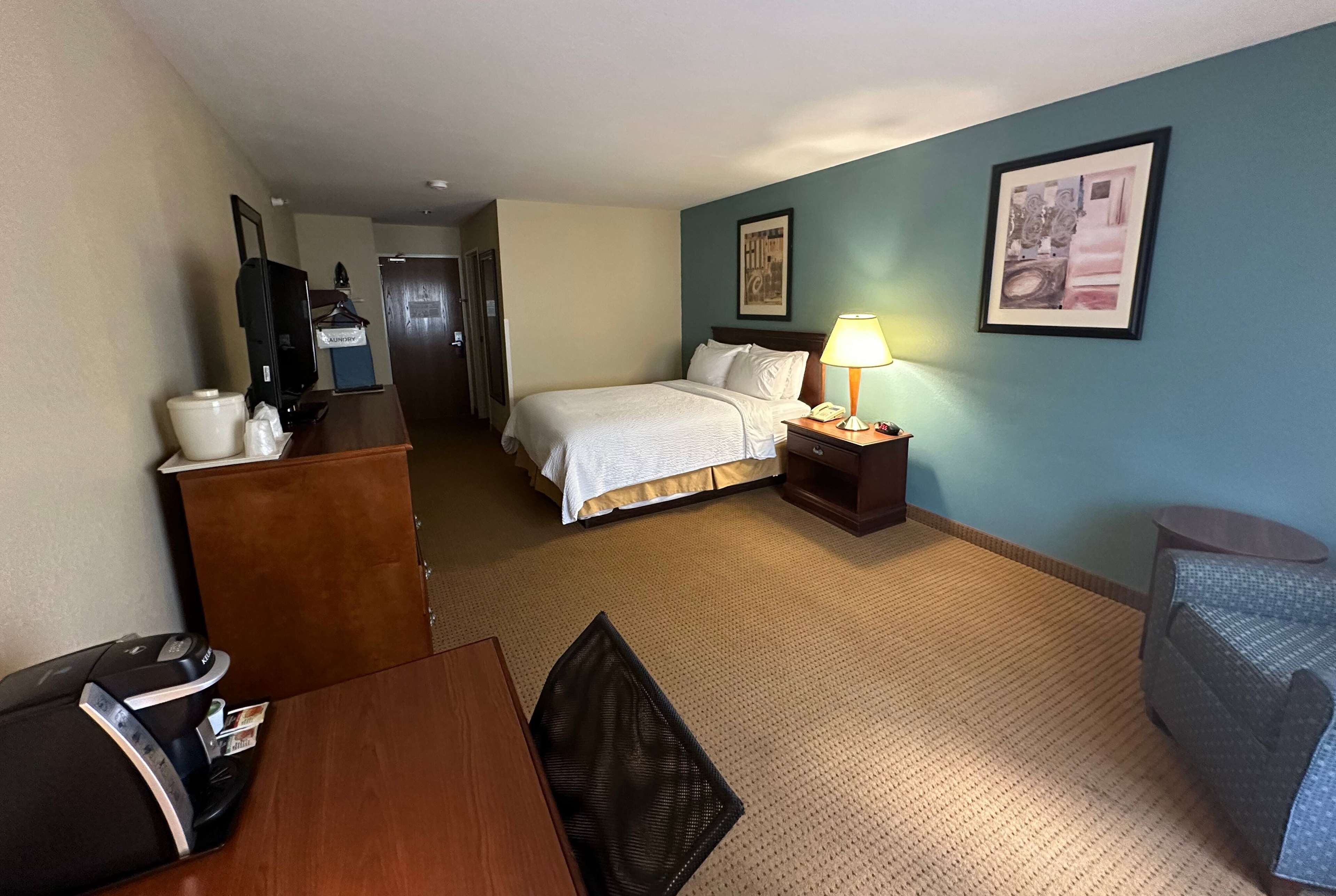 Ein Hotelzimmer mit Bett, Schreibtisch, Stuhl, Lampe und Fernseher.