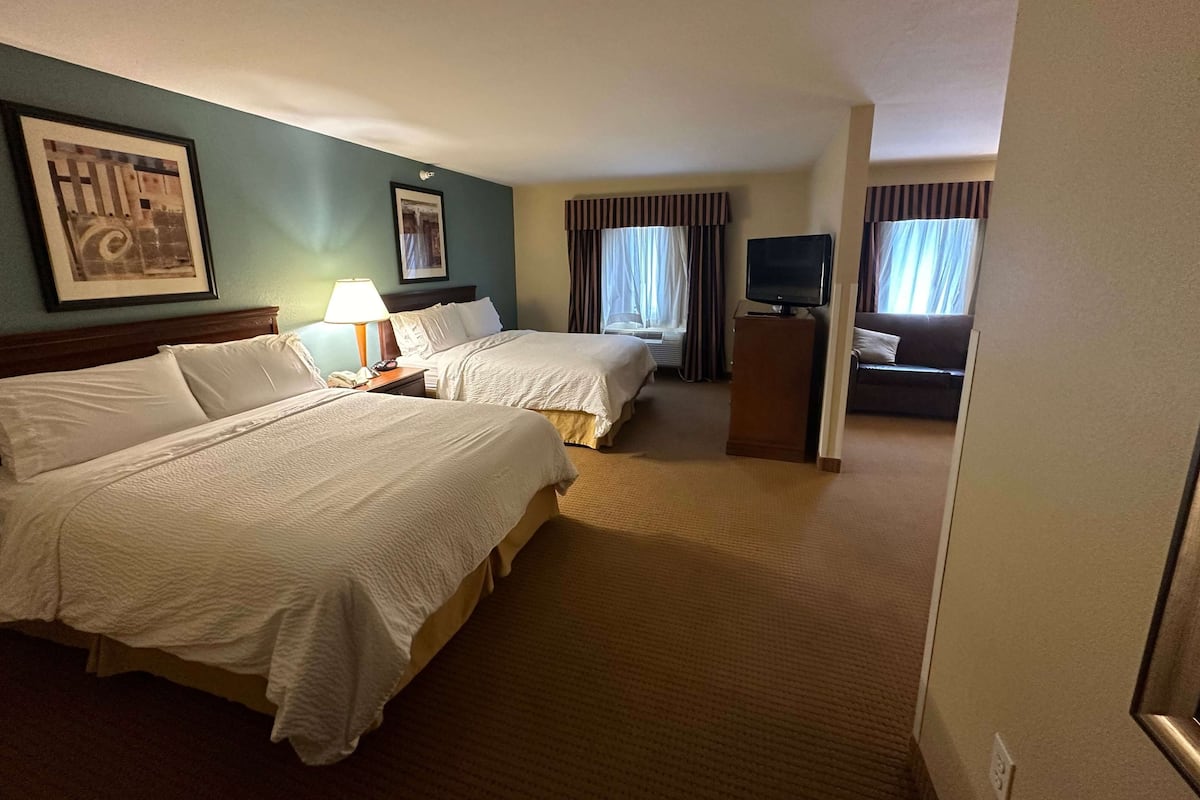 A hotel room with two beds, a desk with a lamp, a television, and a window with curtains.