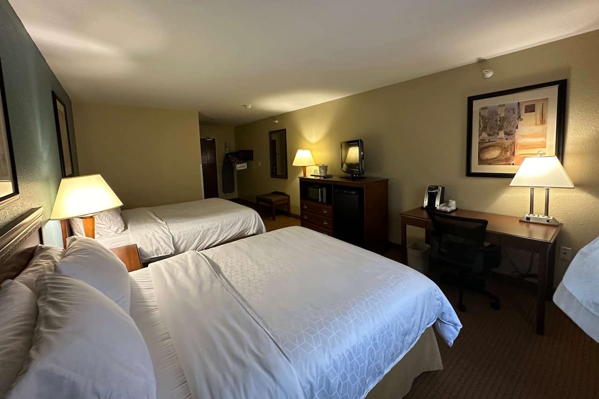 A hotel room with two beds, a desk, a chair, a dresser, and a desk lamp.