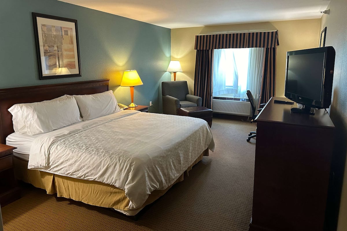 A hotel room with a large bed, a desk with a computer, a chair, and a TV.