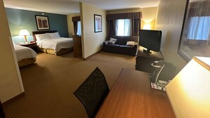 A hotel room with two beds, a sofa, a dining table, and a TV.