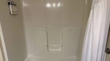 A white shower stall with a shower curtain and a soap dispenser mounted on the wall.