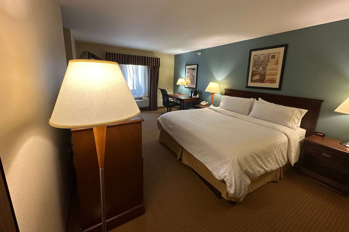 A hotel room with a large bed, a desk with a chair, two bedside lamps, a desk lamp, and a framed picture on the wall.