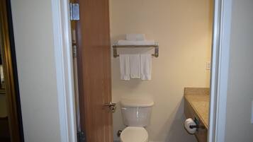 Uma casa de banho com sanita, um porta-toalhas com toalhas e um rolo de papel higiénico.