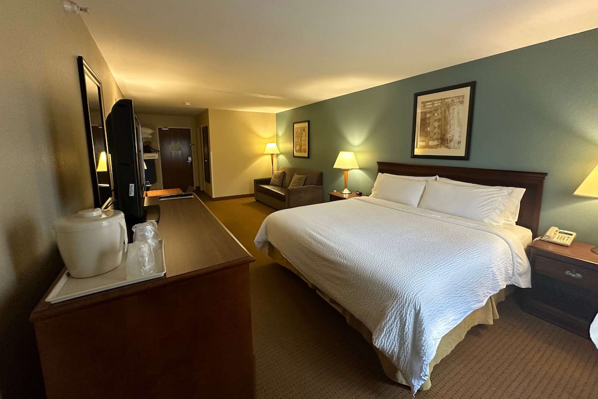 A hotel room with a large bed, bedside tables, a desk with a lamp, a chair, and a mirror.