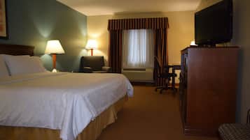 A hotel room with a large bed, a desk with a television, a chair, and a desk lamp.