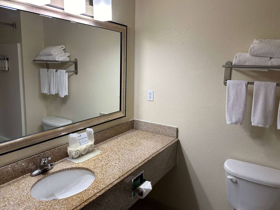 A bathroom with a granite countertop, a sink, a mirror, a towel rack, and a toilet.