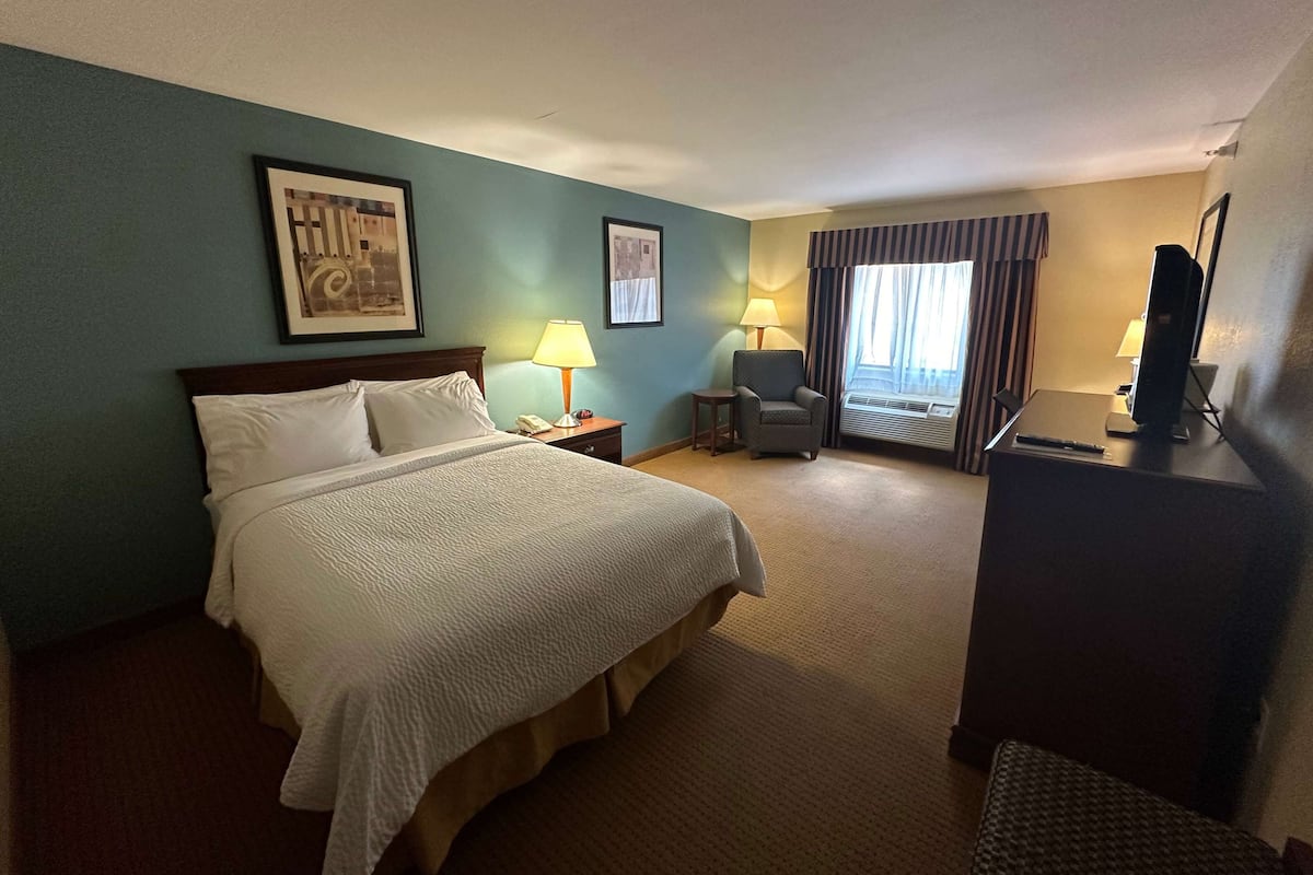 A hotel room with a bed, two bedside tables with lamps, a chair, a desk with a computer, and a TV.
