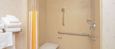 A shower area with a grab bar, a white bench, and towels stacked on a rack.
