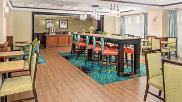 A hotel dining area with a long communal table, multiple bar stools, and several individual tables.