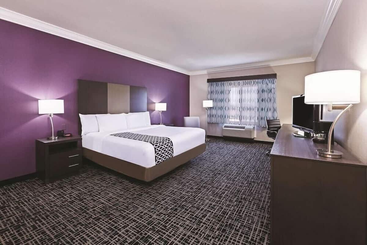 A hotel room with a large bed, two bedside tables with lamps, a desk with a TV, and a window with curtains.