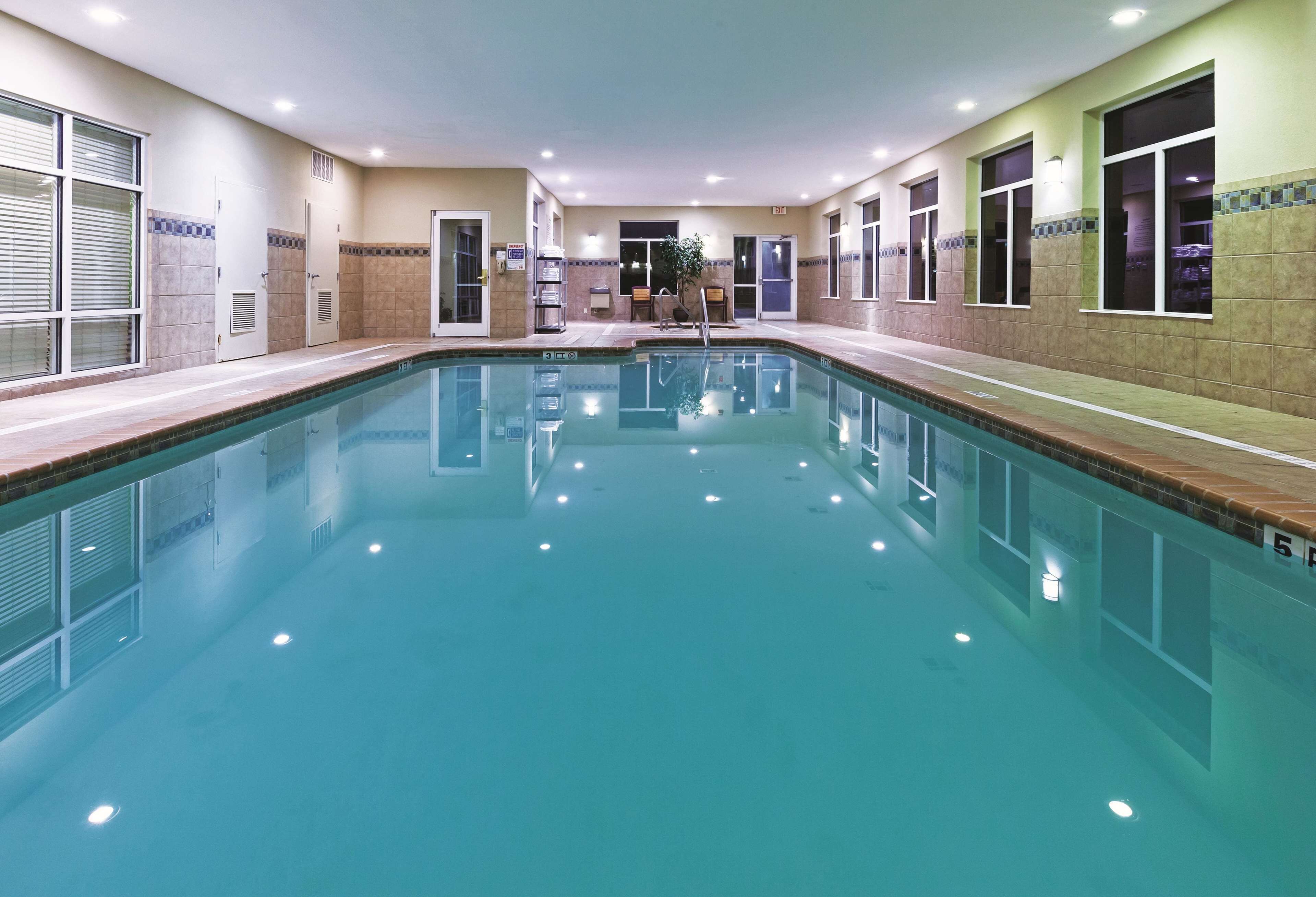A large indoor swimming pool with clear water, surrounded by tiled walls and windows.