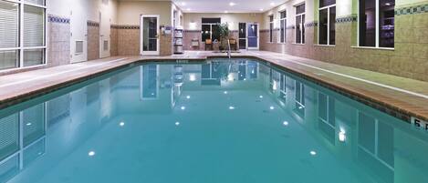 A large indoor swimming pool with clear water, surrounded by tiled walls and windows.