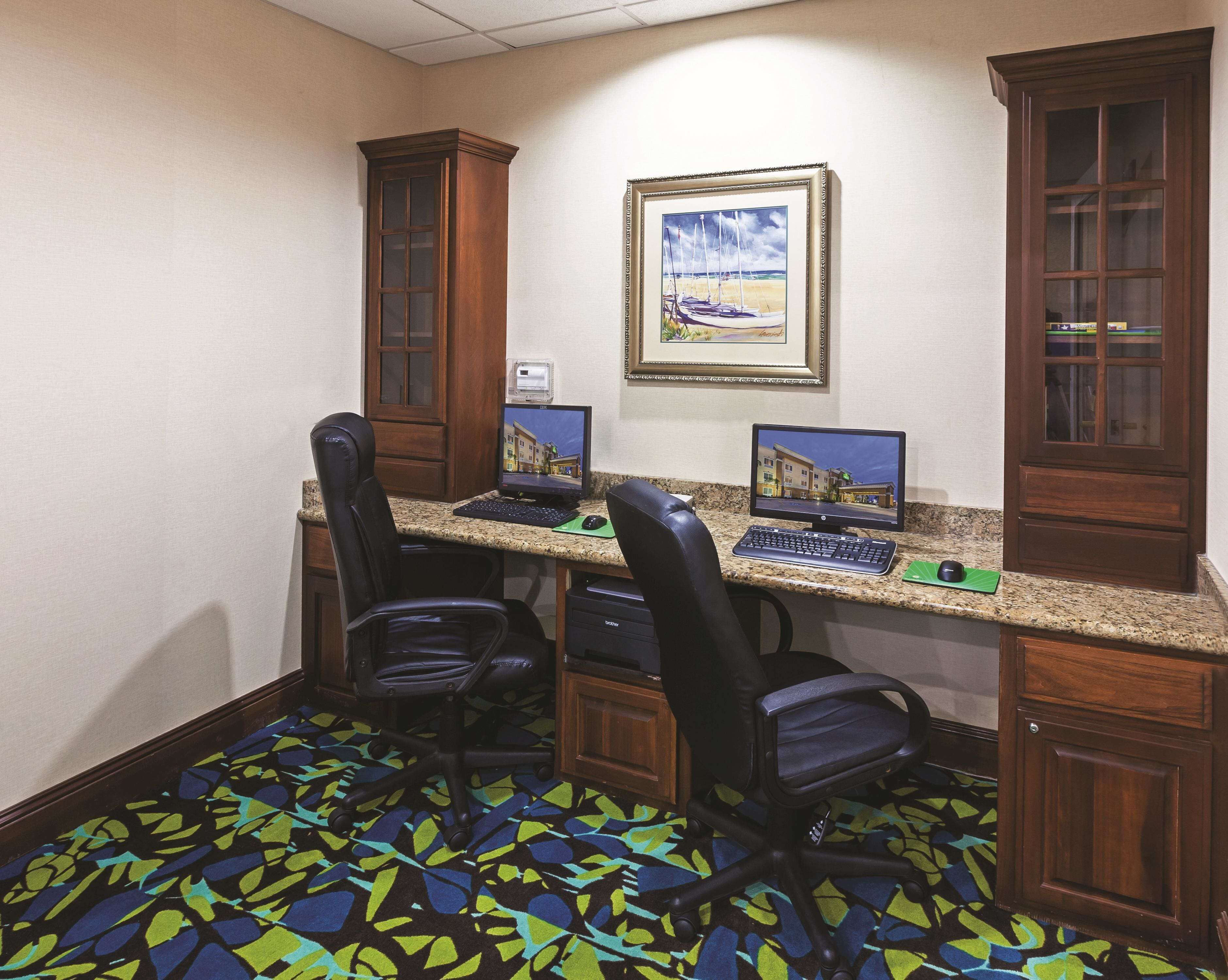 A hotel room with two desks, each with a computer, two black office chairs, and a patterned carpet.