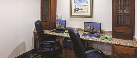 A hotel room with two desks, each with a computer, two black office chairs, and a patterned carpet.