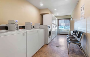 A laundry facility with multiple washing machines and dryers, a row of chairs, and a tiled floor.