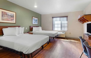A hotel room with two beds, a desk, a chair, a TV, and a window with blinds.