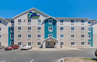 A multi-story hotel with a flat roof, a central entrance, and a parking lot with cars.