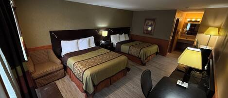 A hotel room with two beds, a desk, a chair, a lamp, and a small table.
