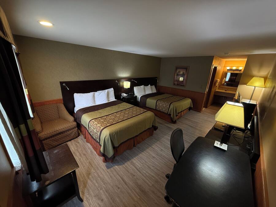 Quarto de hotel com duas camas, uma escrivaninha, uma cadeira, um abajur e uma mesinha.