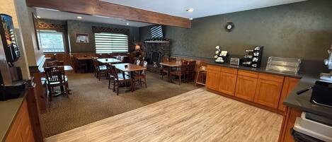 A restaurant with wooden tables and chairs, a counter with a coffee machine, and a stone fireplace.